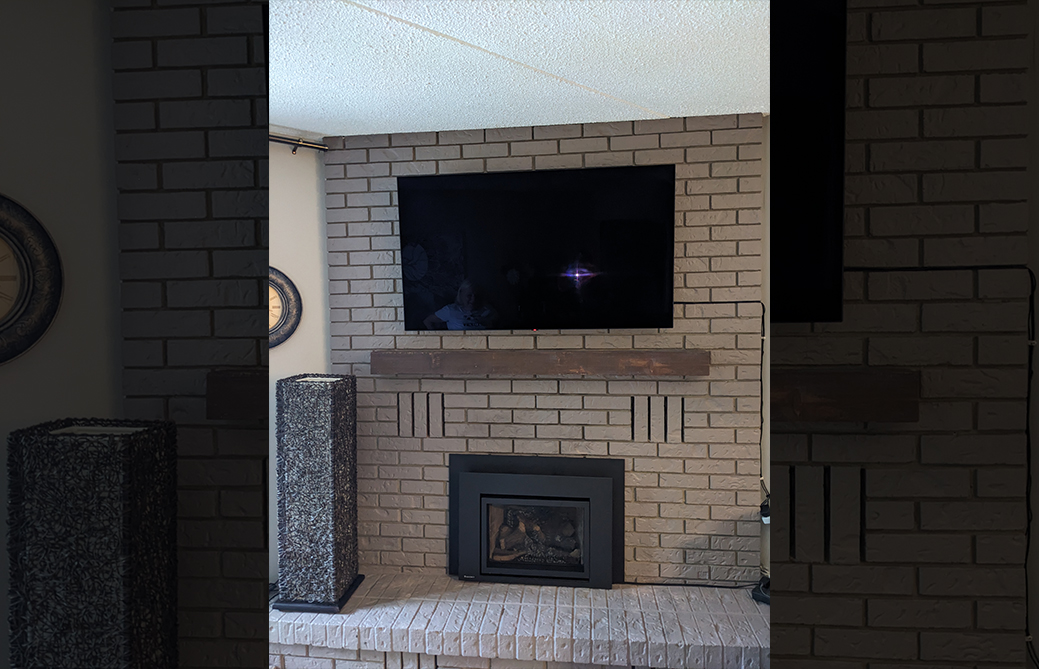 White brick gas fireplace insert with wood mantel and mounted TV