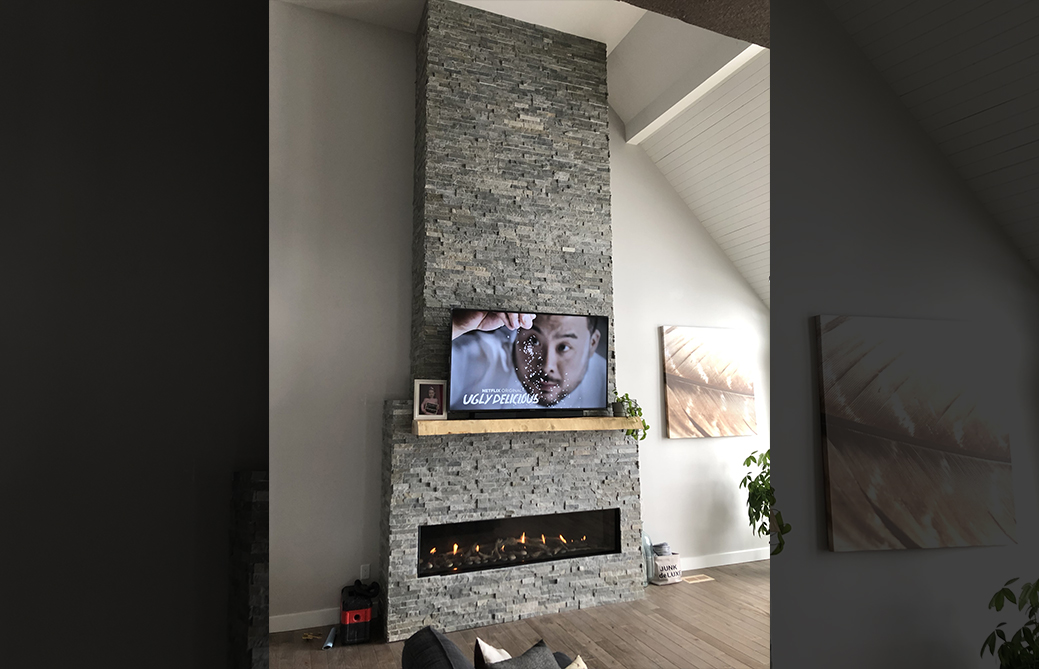 Floor-to-ceiling grey stacked stone linear gas fireplace under cathedral ceiling